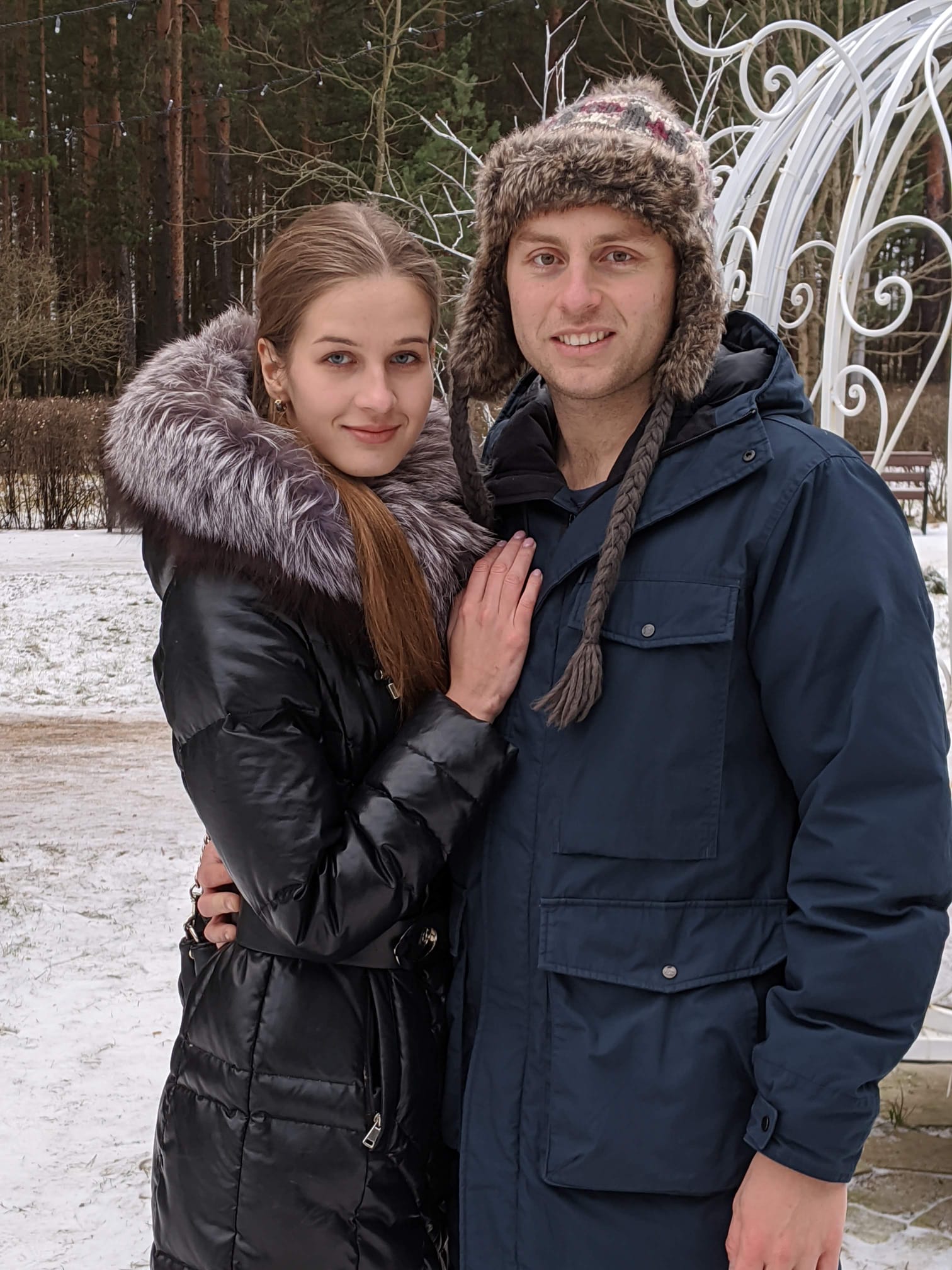 Elena and Louis warmly dressed in the snow among the pines